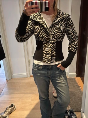 Zebramönstrad cardigan jacka - Snygg zebramönstrad cardigan jacka med bred krage och långa ärmar. Jackan har en figurnära passform och knappar framtill. Köpt i Paris vintage för 900 kr, säljs för 600 kr. Inga defekter. Zebratyget är Manchester ❣️ Jag är 170 lång 