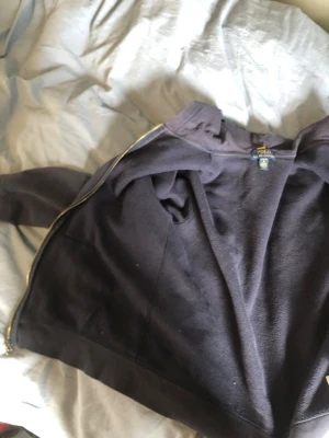 Mörkblå hoodie från Polo Ralph Lauren - Mörkblå hoodie med dragkedja från Polo Ralph Lauren.Klassisk design med huva och mjukt material på insidan. Perfekt för en avslappnad och stilren look. Guldiga detaljer på dragkedjan ger en snygg kontrast. Skriv gärna om du vill ha den den är för barn till 12-14 unegfär 😁