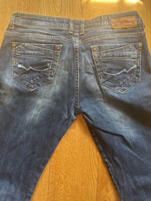 Mörkblå slim fit jeans med slitningar - Snygga mörkblå slim fit jeans med diskreta slitningar och tvättade detaljer på låren och knäna. Klassisk femficksmodell med raka ben och låg midja. Jeansen har dekorativa sömmar på bakfickorna och är tillverkade i stretchigt denimtyg för extra komfort. Slitage på sömmarna mellan benen