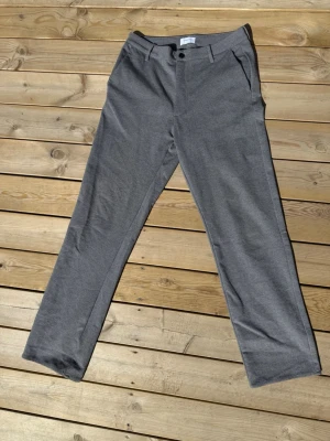 Grå kostymbyxor Studio Total L - Snygga grå kostymbyxor från Studio Total i storlek L. Byxorna har raka ben, diskreta sidofickor och en klassisk knappstängning framtill. Materialet är mjukt och har en lätt struktur som ger en stilren look.