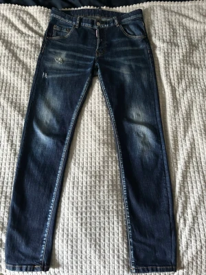 Blå jeans från Dsquared2 - Säljer ett par blå jeans från Dsquared2 med slitningar och detaljerad tvätt. Jeansen har klassisk femficksdesign, kontrastsömmar och en smal passform. Materialet är denim och färgen är mörkblå med ljusare partier och distressed look.