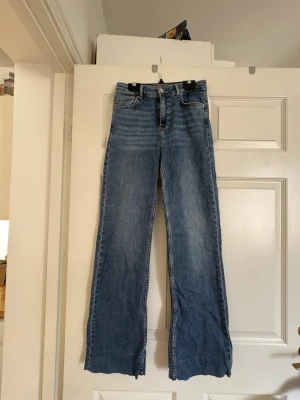 Blå raka jeans - Jeansen har fem fickor, bälteshällor och stängs med knapp och dragkedja. Jeansen är uppsydda men inte avklippta så går också att ta tillbaka till ursprunglig längd