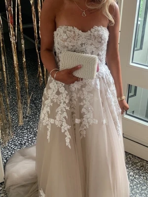 Exklusiv balklänning i spets och tyll - En fantastisk balklänning/klänning i romantisk stil med vackra spetsdetaljer. Klänningen har en figurnära, axelbandlös överdel med broderad spets och en luftig tyllkjol som faller fint. Snörning i ryggen gör att passformen enkelt kan justeras. Modellen på bilden är 172 cm lång, klänningen är anpassad för liknande längd med klackar. Passar till storlek XS-M. En perfekt klänning till bal, student, bröllop eller  andra festliga tillfällen. Nypris ca 7000kr.