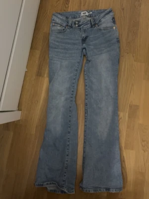 Ljusblå bootcut jeans från 157 - Säljer ett par ljusblå bootcut jeans från 157 med klassisk femficksdesign och dubbla knappar i midjan. Jeansen har en snygg tvättad look och är tillverkade i denim med stretch för extra komfort. Perfekta för dig som gillar en avslappnad och trendig stil.