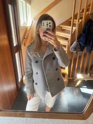 Grå dubbelknäppt rock med hög krage - Grå kort rock med dubbelknäppning och svarta knappar. Från HM i storlek 40, missfärgning vid en av knapparna (se sista bilden) men inget man tänker på 🌻