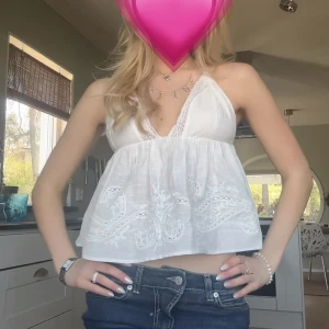 Vit broderad linnetopp med spets - Säljer en vit linnetopp med broderade detaljer och spets längs v-ringningen. Toppen är ärmlös med tunna axelband och har en croppad passform. Perfekt för varma dagar och enkel att matcha med jeans eller kjol. Jag själv har knutit banden då de var för långa för mig