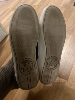 Bruna Michael kors sneakers med logga - Snygga bruna sneakers från Michael Kors med guldfärgad MK-logga på tån och mönstrad ovandel. Skorna har vita kanter och en låg profil. Perfekt för dig som vill ha en trendig och stilren look. Pris kan diskuteras vid snabba köp! 😊