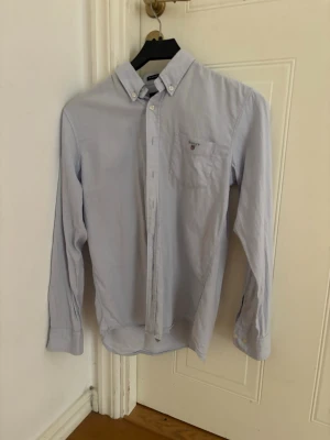 Gant skjorta  - Ljusblå skjorta från GANT i modellen The Archive Oxford. Klassisk och stilren button-down krage med broderad logga på bröstfickan. Perfekt till både vardag, skola och finare tillfällen.  Storlek: 158/164 cm (13–14 years) Färg: Ljusblå Skick: Bra begagnat skick, normal användning förekommer.  Säljes då den inte längre används. Hör av dig vid frågor eller intresse!