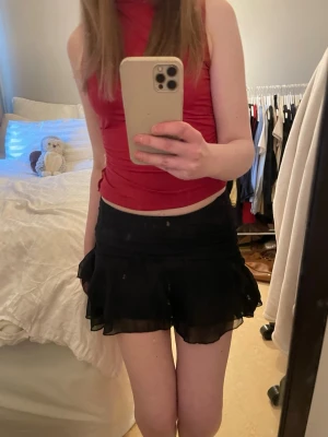 Svart volangkjol med mesh - Säljer en svart kjol med volang och mesh-material som ger ett flowigt och lätt intryck. Kjolen har en kort och luftig design med flera lager som skapar en snygg siluett. Perfekt för dig som gillar trendiga och feminina plagg.