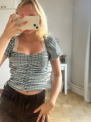 Rutig croppad topp med spetsdetalj💖💖🥹 - Snygg svartvit rutig topp med korta ärmar och croppad passform. Toppen har en söt spetskant vid urringningen och rynkade detaljer framtill. Perfekt för dig som gillar trendiga och feminina plagg.