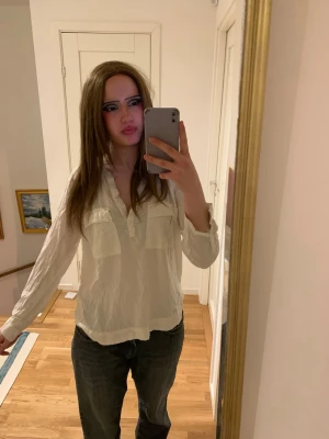 Vit långärmad skjorta med knappar - Säljer en vit skjorta med lång ärm och knappar framtill. Skjortan har två bröstfickor och en avslappnad passform som är perfekt för en chill look. Materialet ser ut att vara bomull och skjortan är enkel att matcha med jeans eller andra byxor.