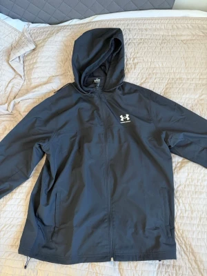 Svart vindjacka från Under Armour - XL - Snygg svart vindjacka från Under Armour med huva och dragkedja framtill. Perfekt för en sommar kväll - knappt använd