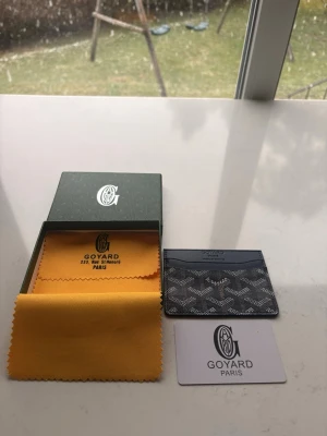 Blått kort fodral  - Säljer ett stilrent svart kortfodral med klassiskt mönster och logotyp. Fodralet är tillverkat i läder och har flera fack för kort. Medföljer originalask, putsduk och autenticitetskort. Perfekt för dig som vill ha något exklusivt och snyggt.