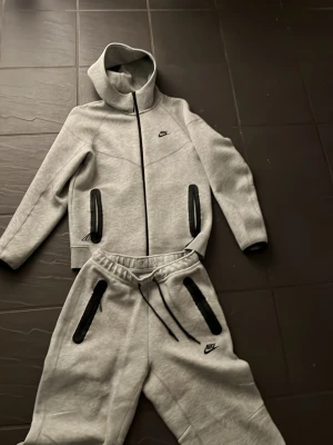 Nike Tech Fleece grå - Grå Nike Tech Fleece mjukisbyxor och zip hoodie med svarta dragkedjor på fickorna och justerbar midja.
