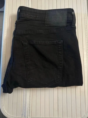 Svarta  jeans Slim/Glenn Superstretch  - Säljer ett par svarta jeans från Jack&Jones i modellen Slim/Glenn och har märkning med superstretch. Jeansen har en diskret patch på linningen och är tillverkade i denim. Perfekta för dig som gillar en enkel och stilren look.