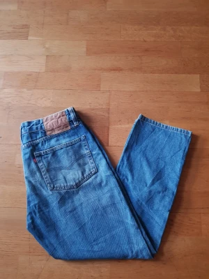Levi's 505 - Klassiska blå Levi's 505 jeans med rak passform och femficksdesign. Jeansen har en tydlig läderpatch bak i midjan och den ikoniska röda Levi's-taggen på bakfickan. Tillverkade i slitstark bomullsdenim, perfekta för en avslappnad och tidlös look.