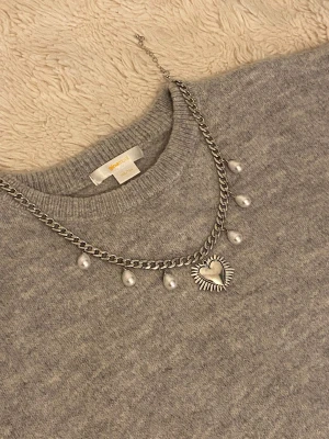 Silverfärgat halsband med pärlor och hjärta - Snyggt silverfärgat halsband från Gina Tricot med droppformade vita pärlor och ett dekorativt hjärthänge i mitten. Kedjan är grov och ger en cool kontrast till de eleganta pärlorna. Perfekt accessoar för att lyfta din outfit.