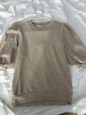 Beige tröja med puffärm från H&M - Mjuk beige tröja från H&M med trendiga puffärmar och rund halsringning. Tröjan har trekvartsärmar och är gjord i ett skönt, stretchigt material som känns lyxigt mot huden. Perfekt för dig som gillar en clean och stilren look.