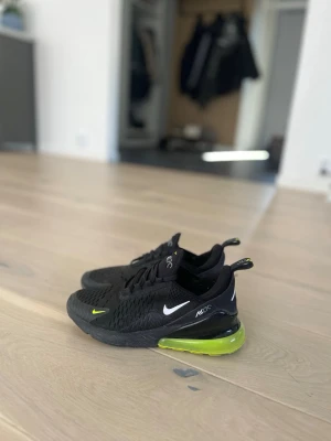 Nike Air Max 270 svart/lime sneakers - Snygga Nike Air Max 270 sneakers i svart mesh med vita loggor och limegröna detaljer på sulan. Skorna har en chunky design med synlig Air Max-dämpning i hälen och klassiska snörningar. Perfekta för dig som gillar sportig stil och coola färgkombinationer. pris kan diskuteras