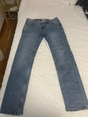 Blå raka jeans från 157 - Säljer ett par klassiska blå jeans från 157 med raka ben och femficksdesign. Jeansen har normal midja och snygga slitningar som ger en cool look. Perfekta för dig som gillar en enkel och tidlös stil.