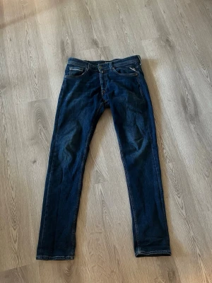 Mörkblå jeans från replay - Säljer ett par mörkblå slim fit jeans från replay med klassiska femficksdetaljer och snygga kontrastsömmar. Jeansen har en rak passform och är tillverkade i slitstarkt denim. Perfekt för dig som gillar en tidlös och clean look.