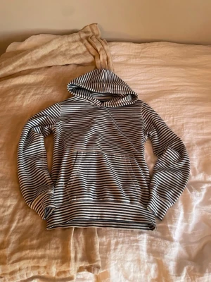 Randig hoodie i svart och vitt - Snygg hoodie med blåvita horisontella ränder och huva. Tillverkad i mjukt och stretchigt material som känns skönt mot huden. Perfekt för dig som gillar en avslappnad och stilren look. Långa ärmar och klassisk passform.