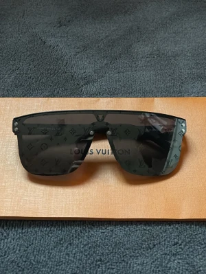 Lv glasögon - Louis Vuitton Solglasögon – Monogram Lens  Exklusiva solglasögon från Louis Vuitton med ikoniskt monogrammönster ingraverat i glasen. Modern shield-design som ger en kraftfull och lyxig look.  Perfekt statement-accessoar för dig som vill sticka ut med stil och kvalitet i toppklass.  Skick: nytt skick!