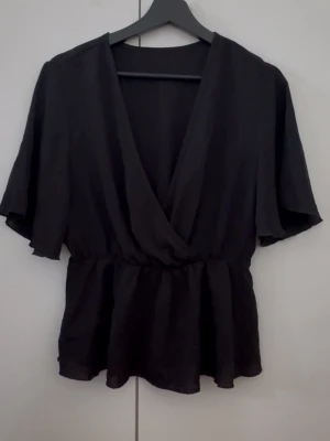 Svart omlottopp med v-ringning - Svart volang med v-ringning och vida korta ärmar. Midjan ger ett snyggt flowy fall. Priset för att jag vill bli av med den och inte slänga plus att den e super fin! höjer priset om den inte säljs snart‼️‼️ 