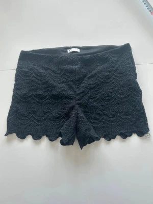 Svarta spets-shorts - Säljer ett par svarta shorts med snygg spets och scallop-detaljer längst ner. De har en midwaist passform och är perfekta för dig som gillar en feminin och trendig stil. 
