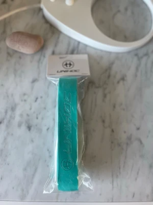 Turkost bälte från Unihoc - Snyggt turkost bälte från Unihoc med präglad logga längs hela bandet. Perfekt accessoar för dig som vill addera lite färg till din outfit. Bältet är tillverkat i syntetmaterial och har en modern, sportig look.