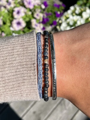 Armband set  - Säljer ett snyggt set med tre armband: ett i flätad blåvitt textil, ett med svarta och beige pärlor samt ett stelt silverfärgat armband med ingraverade detaljer. Perfekt för dig som gillar att mixa olika stilar och material. Alla armband är justerbara och sitter inte ihop men säljs som ett set. Perfekt till sommaren☀️