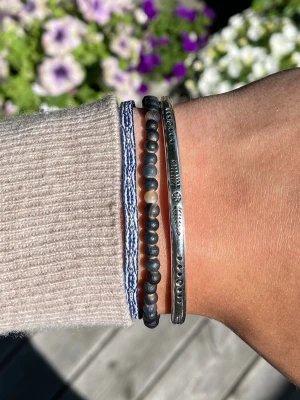 Armbands det - Säljer ett set med tre armband: ett med mörka pärlor i svart och beige toner, ett i blåvitt flätat band och ett i silverfärgad metall med ingraverade detaljer. Perfekt för dig som gillar att mixa olika stilar och material. Alla armband är justerbara och sitter inte ihop men säljs som ett set. Perfekt till sommaren☀️