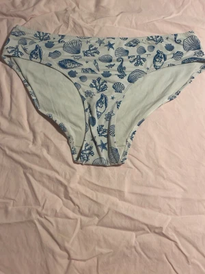 Bikini underdel med havsmotiv - En vit bikini underdel med blå havsmotiv såsom snäckor, stjöstjärnor och koraller. Köpt på Lindex och är i storlek 170, säljer tyvärr bara underdelen! Välanvänd men fint skick 🥰
