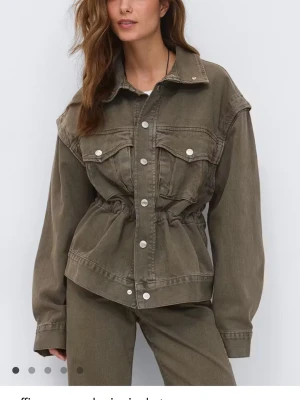 Olivgrön jeansjacka med fickor - Snygg olivgrön jeansjacka med markerad midja och silverfärgade knappar. Jackan har två bröstfickor med lock och knapp samt klassisk krage. Tillverkad i kraftigt jeansmaterial och har en avslappnad passform.