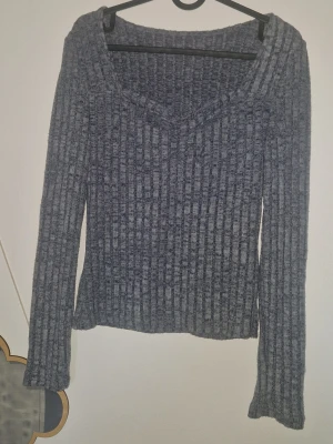 Ribbstickad tröja med V-ringning - Mysig grå stickad tröja med ribbad struktur och V-ringad hals. Tröjan har långa ärmar och en avslappnad passform som gör den perfekt för kyliga dagar. Materialet känns mjukt och stretchigt, vilket ger en skön känsla hela dagen.