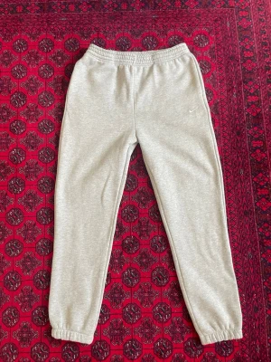 Grå mjukisbyxor från Nike - Gråa mjukisbyxor från Nike med klassisk vit swoosh-logga på benet. Byxorna har resår i midjan och vid bensluten för en skön passform. Tillverkade i mjukt och bekvämt material, perfekta för chill eller träning.