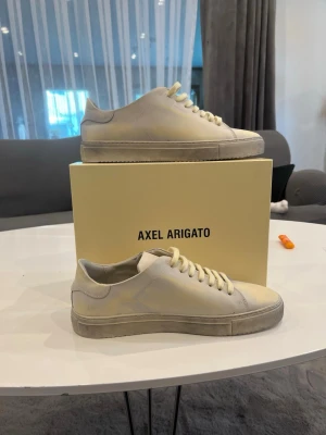 Vita Axel Arigato sneakers i läder - Snygga vita sneakers från Axel Arigato i stilren design. Skorna är låga och tillverkade i slätt läder med matchande vita skosnören och sula. Perfekta för en clean och minimalistisk look.