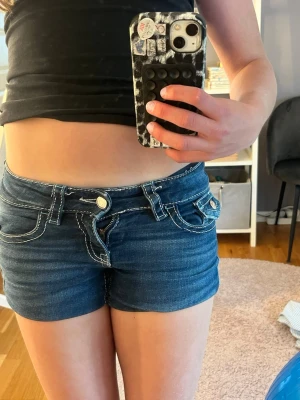 Blå denimshorts med vit söm - Snygga blå denimshorts med kontrasterande vita sömmar och dekorativa fickor både fram och bak. Shortsens design har dubbla knappar och bälteshällor, vilket ger en cool och ungdomlig look. Perfekta för varma dagar och enkel att matcha med olika toppar.