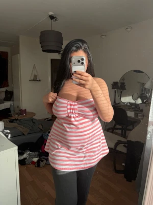 Rosa och vit randig tubtopp - Säljer en söt axelbandslös tubtopp med rosa och vita ränder. Toppen har bandeau-modell och en liten rynkning framtill som ger en snygg detalj. Perfekt för varma dagar och enkel att styla med jeans eller kjol.