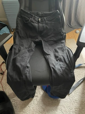 Svarta raka jeans - Säljer ett par svarta jeans med rak passform och klassisk femficksdesign. Jeansen har knappgylf och bälteshällor, perfekta till en avslappnad streetwear-look. Materialet är denim i bomull. Passar dig som gillar stilrena och enkla plagg.