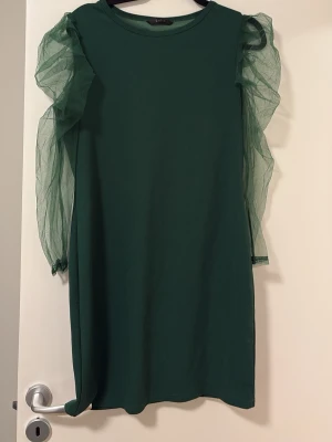 Grön klänning med puffärmar - Snygg grön klänning med transparenta puffärmar i mesh. Rak passform och rund halsringning. Perfekt för dig som vill sticka ut med en unik detalj på ärmarna. Klänningen är enkel men har en cool twist tack vare de voluminösa ärmarna.