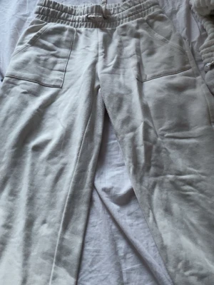 Beiga midwaist mjukisbyxor med fickor - Säljer ett par beiga mjukisbyxor med resår och dragsko i midjan. Byxorna har stora, synliga fickor framtill och är gjorda i ett mjukt, skönt material som känns riktigt chill. Perfekta för en avslappnad look.