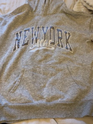Grå hoodie med New York-tryck - Snygg grå hoodie med stor ficka framtill och texten 'NEW YORK’.