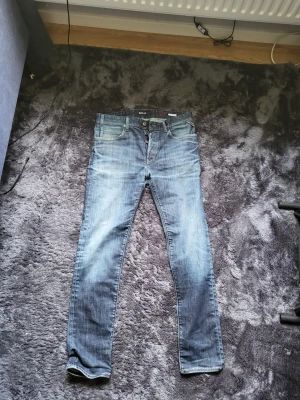 Replay jeans  - Säljer ett par klassiska blå jeans från Replay i rak modell med knappgylf och fem fickor. Jeansen har snygg tvätt med lätt slitning och är tillverkade i denim. Perfekta för dig som gillar en tidlös och avslappnad stil.