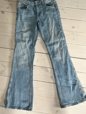 Ljusblå bootcut jeans - Säljer ett par ljusblå bootcut jeans med klassisk femficksdesign och normal midja. Jeansen har en lätt tvättad look och är tillverkade i denim med lite stretch för skön passform. Perfekta för en avslappnad och trendig stil.