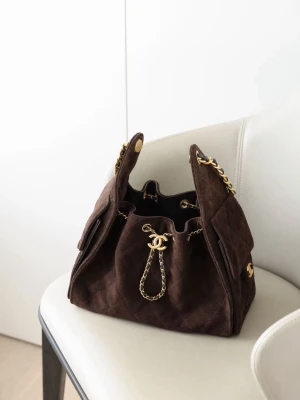 Brun mocka bucket bag - Säljer en brun bucket bag i lyxig mocka med quiltat mönster. Väskan har guldfärgade kedjedetaljer. Dragskostängning och sidofickor ger en cool och trendig look. Perfekt för dig som vill sticka ut med en ikonisk väska.