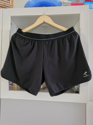 Svarta träningsshorts Energetics 2XL - Svarta träningsshorts från Energetics med elastisk midja och DRYPLUS eco-material som andas. Perfekta för gymmet eller löprundan. Klassisk design utan extra detaljer för en clean look. Inbyggda cykelbyxor
