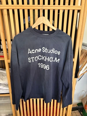 Mörkblå sweatshirt Acne Studios - Mörkblå sweatshirt från Acne Studios med tryck i vitt framtill där det står 'Acne Studios Stockholm 1996'. Tröjan har rund halsringning och långa ärmar. Perfekt för en avslappnad och trendig look. Storlek S och i väldigt fint skick.