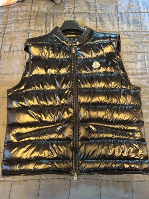 Moncler Väst  - Säljer en fin moncler väst i storlek XXL men den sitter som en XL/Stor L. Den kommer tyvärr inte till användning. Jätte bra skick, knappt använd!!!! 