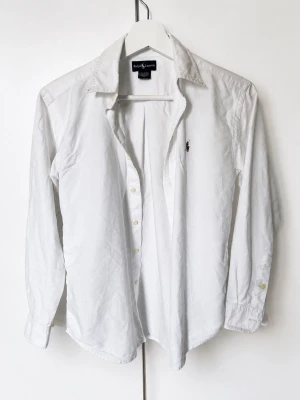 Vit skjorta från Ralph Lauren - Klassisk vit skjorta från Ralph Lauren med broderad logga på bröstet i storlek XS/S. Skjortan har lång ärm, knappar framtill och en tidlös design som passar till allt. Tillverkad i bomull för en skön och luftig känsla. Priset går att diskutera och tveka inte vid minsta fundering!